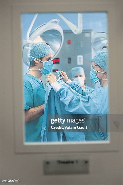 nurse helping a surgeon to get dressed with his surgical scrubs in an operating room - operating room window stock pictures, royalty-free photos & images