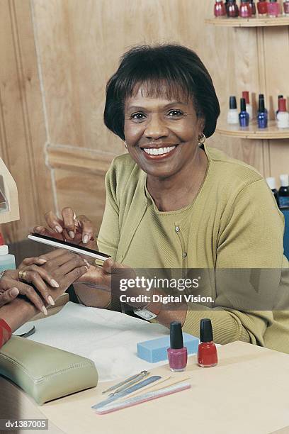 smiling beautician giving another woman a manicure in a beauty salon - beauty salon foto e immagini stock