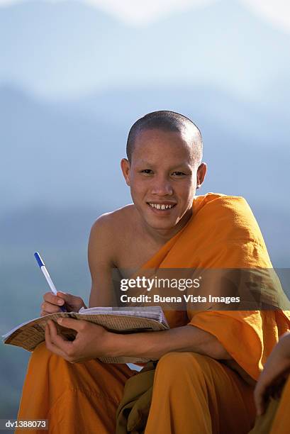 portrait of a monk sitting and holding a pen and a notepad - laotische kultur stock-fotos und bilder