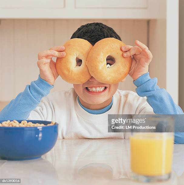portrait of a boy in a kitchen at breakfast looking through holes in bagels - boy pajamas cereal stock pictures, royalty-free photos & images