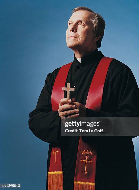 priest standing holding crucifix, spotlit - priest collar stock pictures, royalty-free photos & images