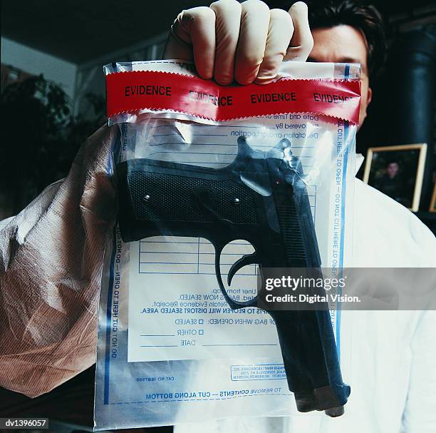 male forensic scientist holding an evidence bag with a gun inside - plastic bag stock pictures, royalty-free photos & images