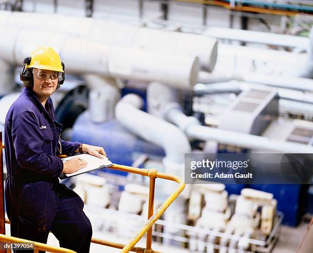 foreman wearing overalls, hard hat and ear defenders stands on a platform in a factory - foreman stock pictures, royalty-free photos & images