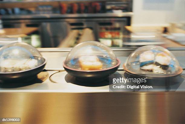 containers of sushi in a line on a conveyor belt in a restaurant - sushi train stock pictures, royalty-free photos & images