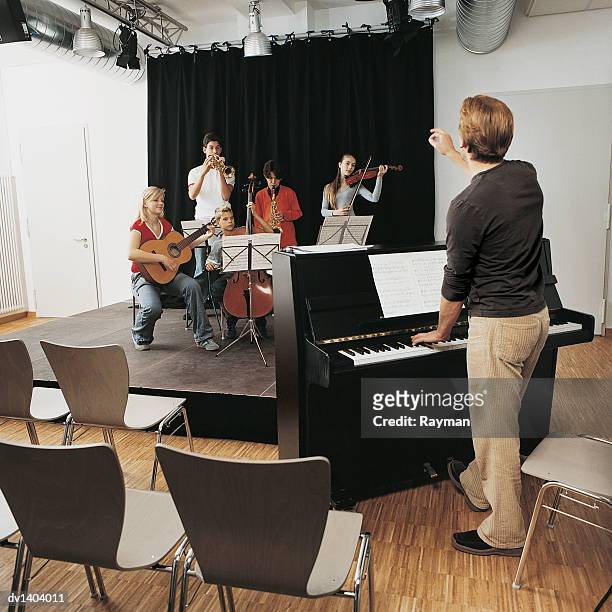 music teacher stands at a piano conducting a school band - girl cello stock pictures, royalty-free photos & images