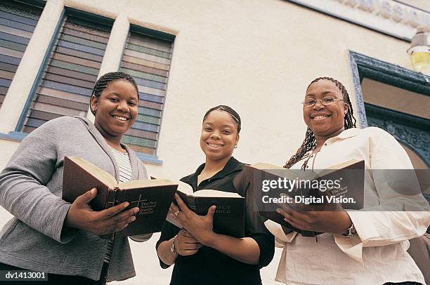 portrait of three smiling, young women standing outside a church with their bibles - african american church stock pictures, royalty-free photos & images