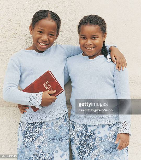 portrait of a young girl holding a bible with her arm around another smiling, young girl - godsdienstvrijheid stockfoto's en -beelden