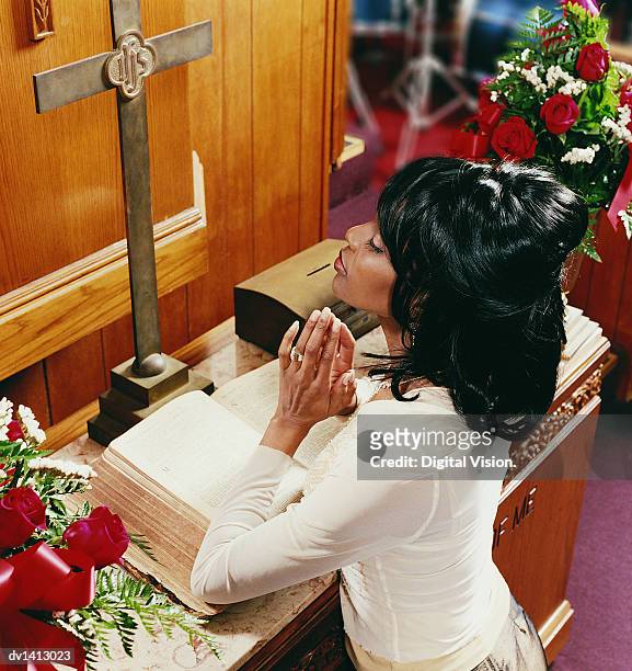young woman kneeling at an altar in church and praying - black women praying stock pictures, royalty-free photos & images