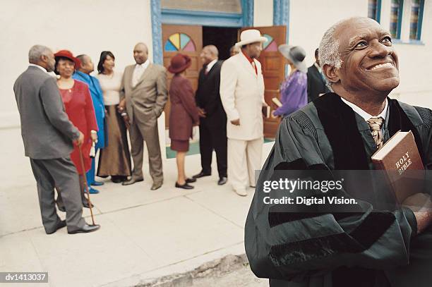 smiling priest standing in front of a group of people outside a church holding a bible - godsdienstvrijheid stockfoto's en -beelden
