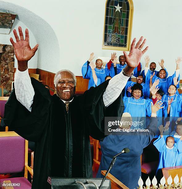 priest standing on a pulpit with his arms upraised in front of a gospel singing choir - música religiosa fotografías e imágenes de stock