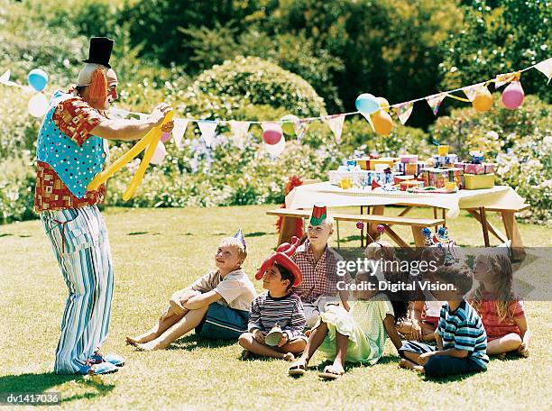 clown entertaining children sitting on the grass at a birthday party - payaso fotografías e imágenes de stock