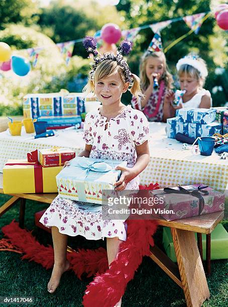 a girl at an open air birthday party, sitting at a table, holding a present - open seat godo stock-fotos und bilder