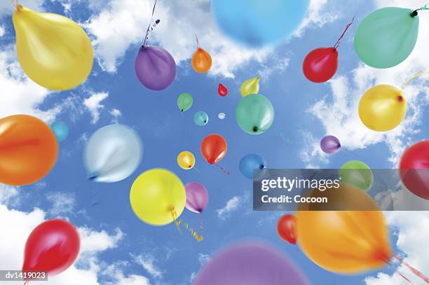 multi-coloured balloons move upwards into a summer sky - balloons in sky stock pictures, royalty-free photos & images