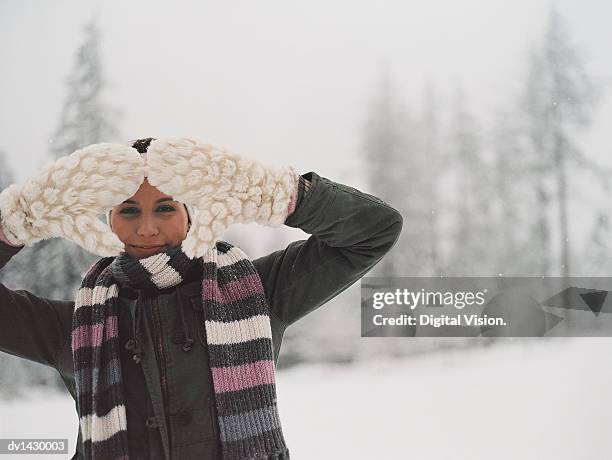 portrait of a young woman outdoors in the snow looking through her mittens - the mittens stockfoto's en -beelden