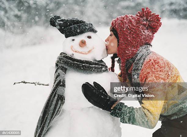 young woman kissing a snowman - frau schneemann stock-fotos und bilder