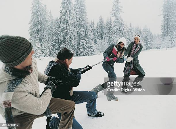 young couples outdoors in the snow playing a game of tug of war - war stock-fotos und bilder