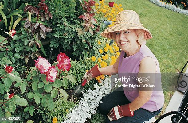 senior woman kneeling on the grass and using a garden trowel by a flowerbed - sleeveless top stock pictures, royalty-free photos & images