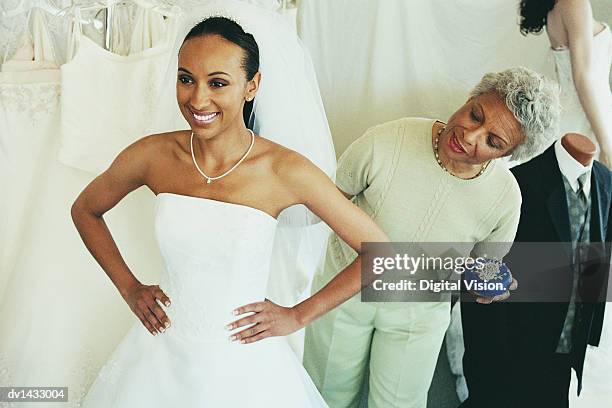 shop assistant helping a woman try on a wedding dress in a clothes shop - bridal shop stockfoto's en -beelden