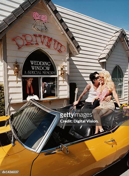 newlywed couple sitting on the backseat of a convertible in front of a wedding chapel and groom kissing bride - las vegas wedding ストックフォトと画像