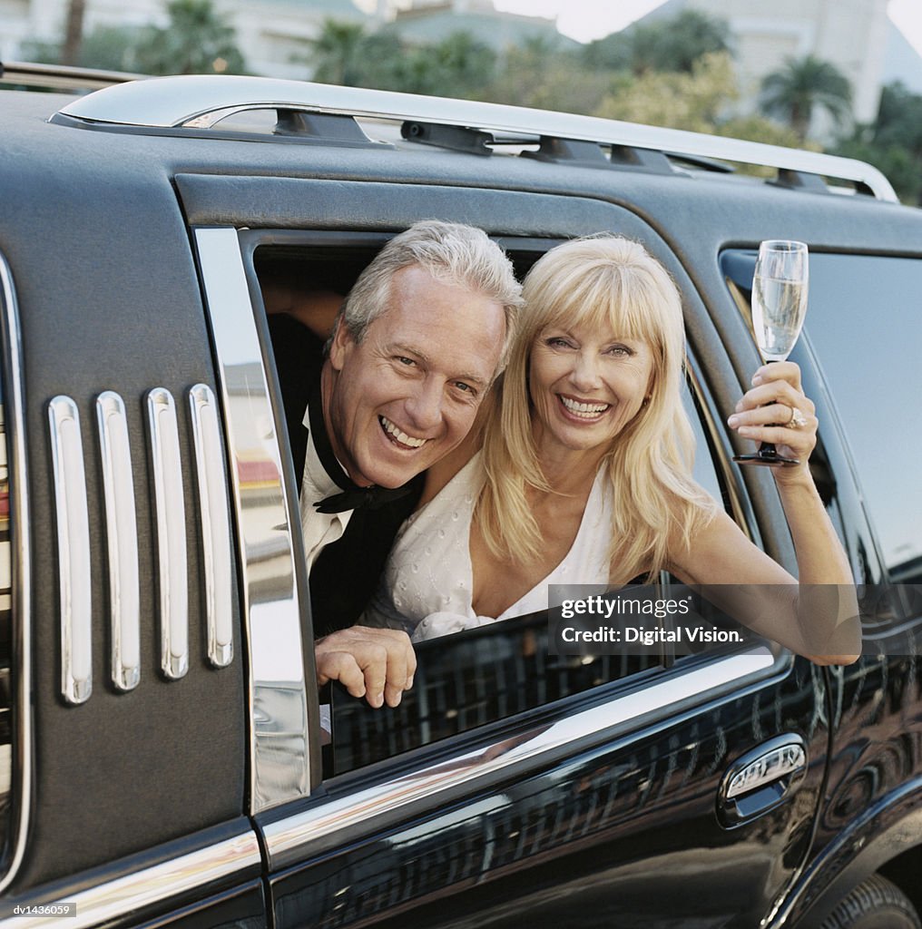 Happy Couple Looking Out of a Limousine Window, the Woman Holding a Champagne Glass