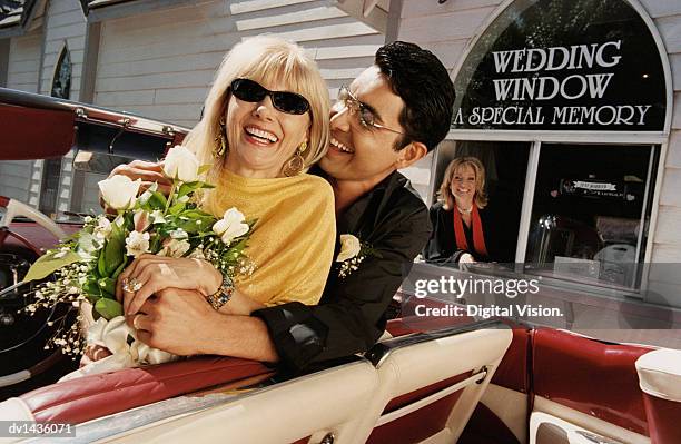 smiling, newlywed couple sitting in the front seat of their convertible by a drive in church - las vegas wedding stock pictures, royalty-free photos & images