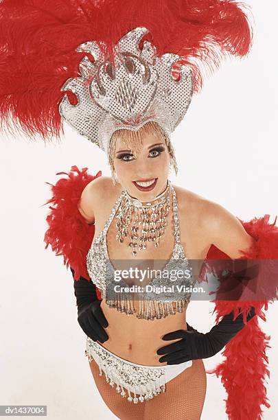 studio portrait of a showgirl with a sequined headdress and feather boa standing with her hands on her hips - chorus line stock-fotos und bilder