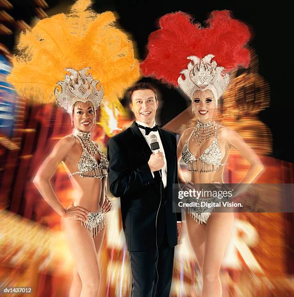 man in a dinner jacket holding a microphone stands between two chorus girls, against a blurred composite background - chorus line stock-fotos und bilder