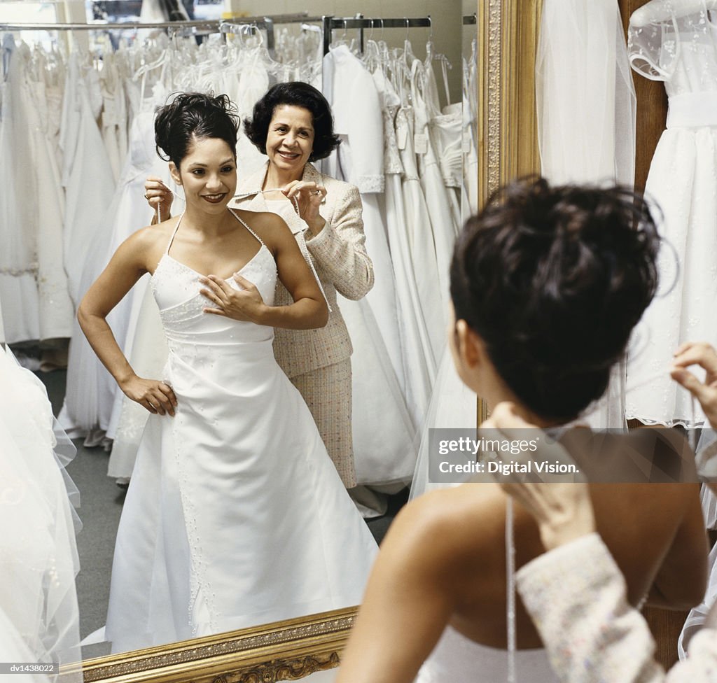Senior Woman Helping Her Daughter Try on a Wedding Dress in Front of a Mirror in a Bridal Shop