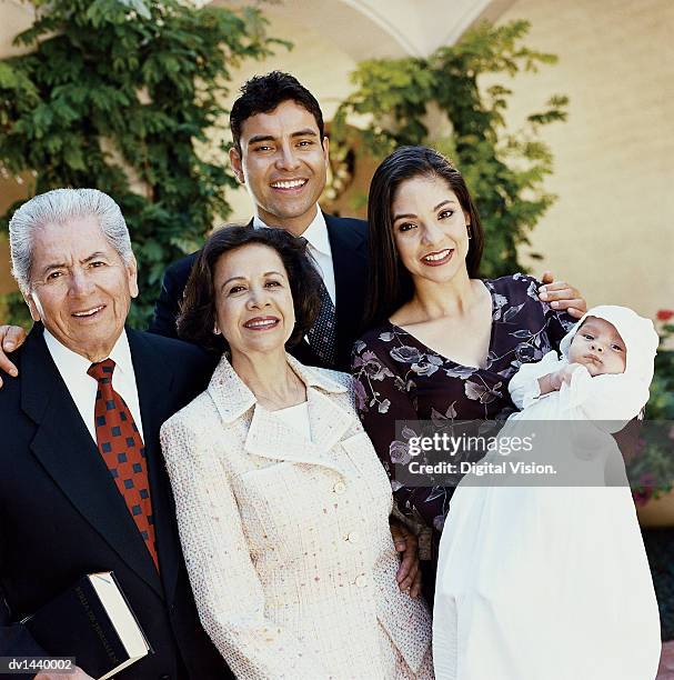 portrait of a family of five at a baptism, mother holds her baby in a christening gown - christening gown stockfoto's en -beelden