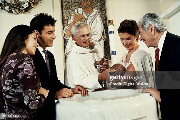 parents and grandparents holding a baby stand around a baptismal font, the priest baptising the baby - pila bautismal fotografías e imágenes de stock