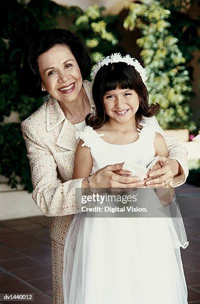 portrait of a grandmother and her young granddaughter in her first communion dress, holding a prayer book - comunion fotografías e imágenes de stock