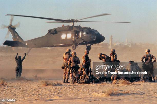 military helicopter landing in desert as group of soldiers watching - war foto e immagini stock