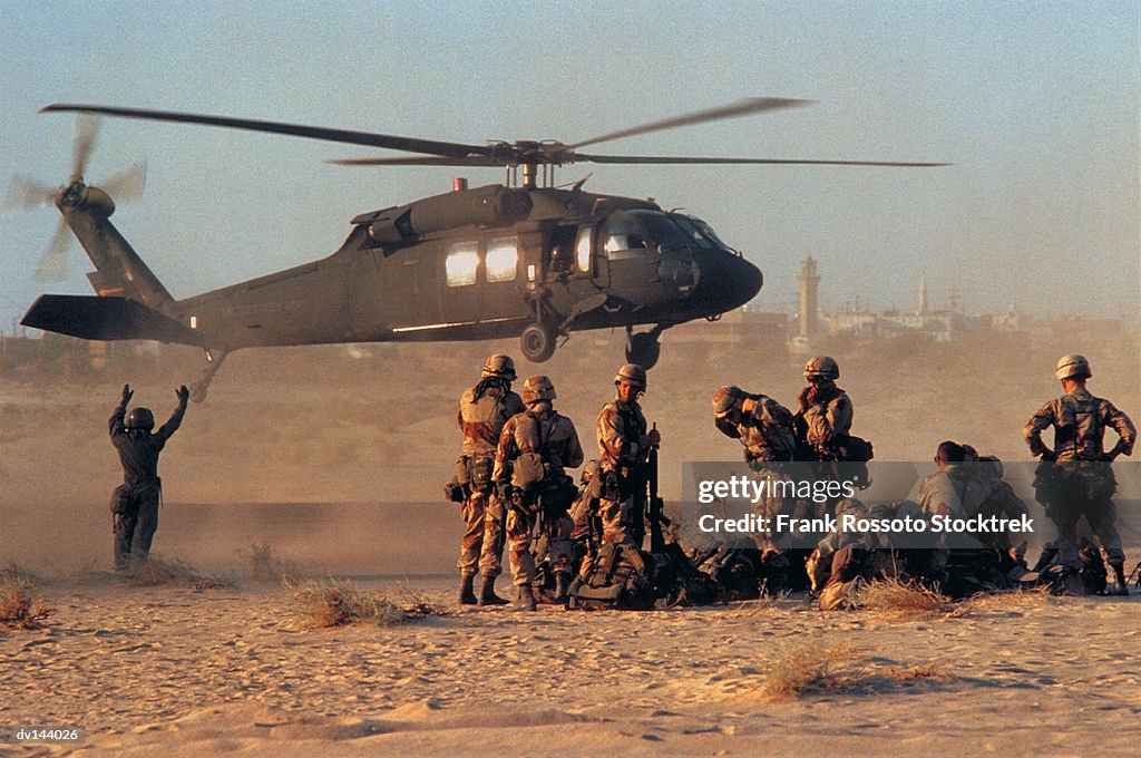 Military helicopter landing in desert as group of soldiers watching