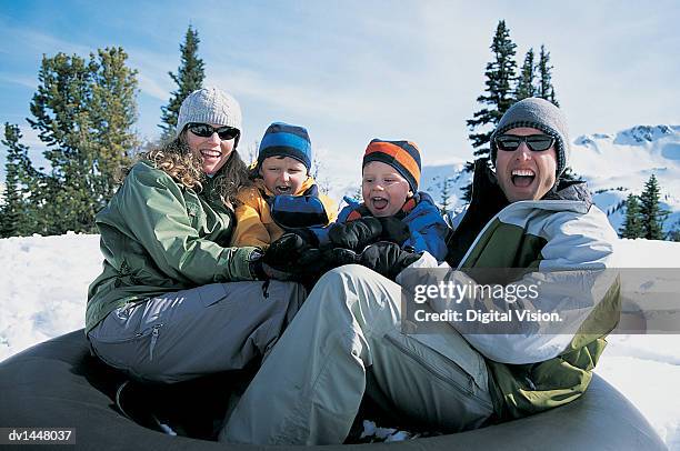 portrait of a smiling family of four sitting on a rubber ring in the snow - rubber ring stock-fotos und bilder