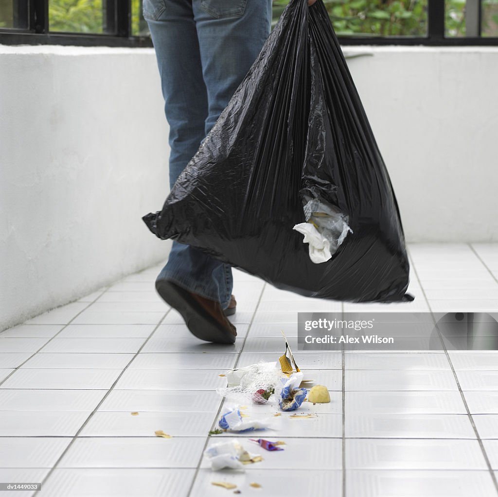 Man Dropping Rubbish on a Tiled Floor From a Hole in a Bin Bag