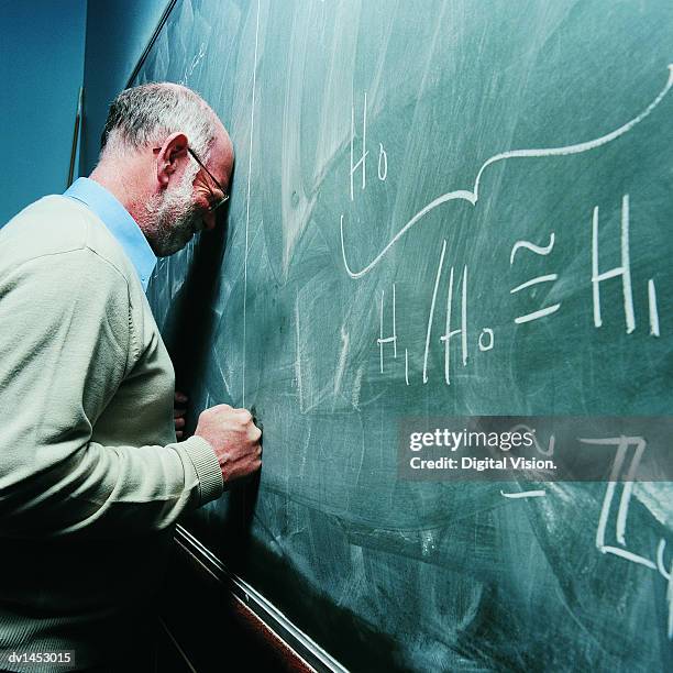 portrait of a frustrated maths lecturer banging his head against a blackboard - overworked teacher stock pictures, royalty-free photos & images