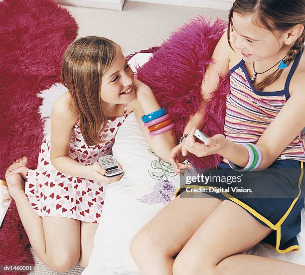 two teenage girls sitting holding mobile phones - heart bracelet stock pictures, royalty-free photos & images