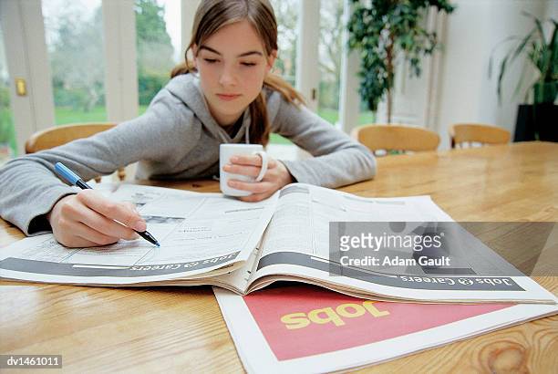 teenage girl sitting behind a table searching for jobs in a newspaper - searching for something ストックフォトと画像