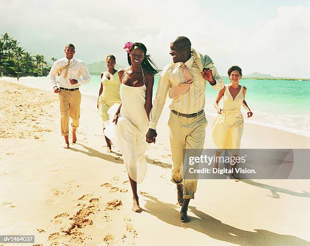 newlywed couple walk on a beach hand-in-hand, accompanied by bridesmaids and best man - african american wedding foto e immagini stock