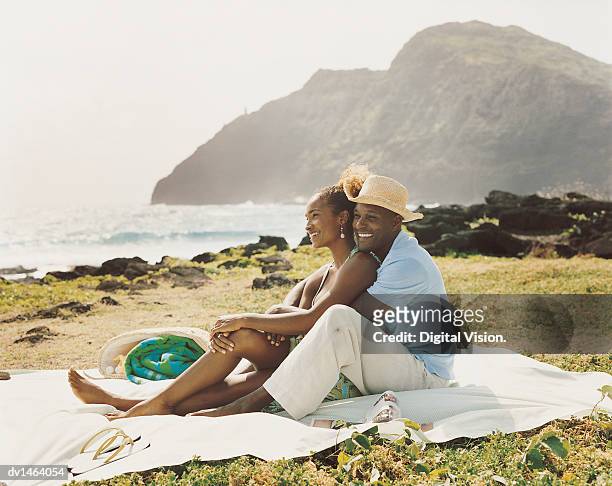 couple sit embracing on a picnic blanket on grass at the coast - cliff side stock pictures, royalty-free photos & images