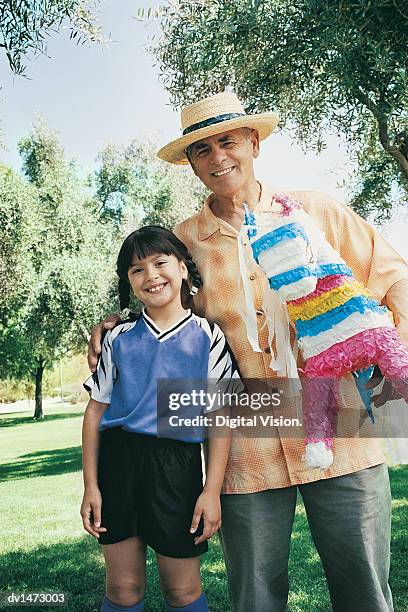 grandfather and grandaughter stand holding a pinata in a park - pinata stock pictures, royalty-free photos & images