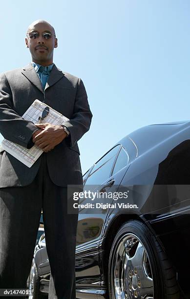 serious car salesman stands next to a black car holding a clipboard - digital devices beside each other bildbanksfoton och bilder