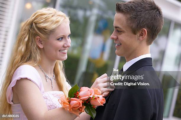 young couple standing face to face dressed for a high school prom, girl adjusting boy's corsage - corsage imagens e fotografias de stock