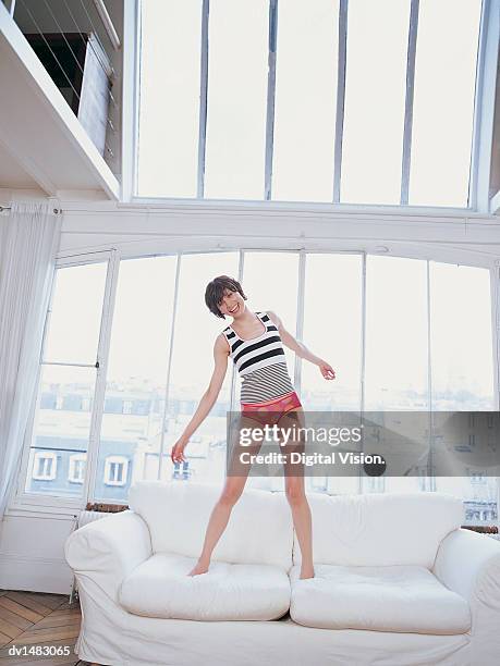young woman bouncing on sofa in apartment with views over rooftops of paris - french knickers stock pictures, royalty-free photos & images