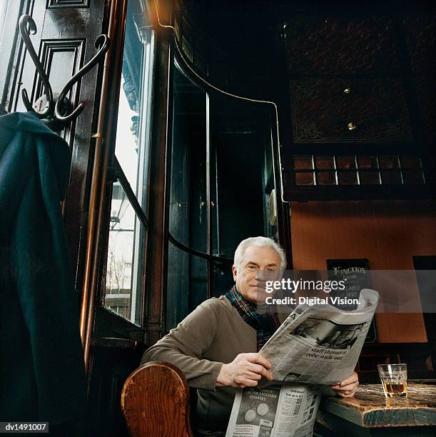 mature man sitting at a table in a pub with a newspaper - bulletin board stockfoto's en -beelden