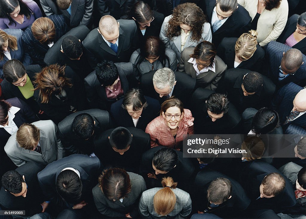 Businesswoman Looking up at Camera and Standing Outdoors Surrounded by a Large Group of Business People