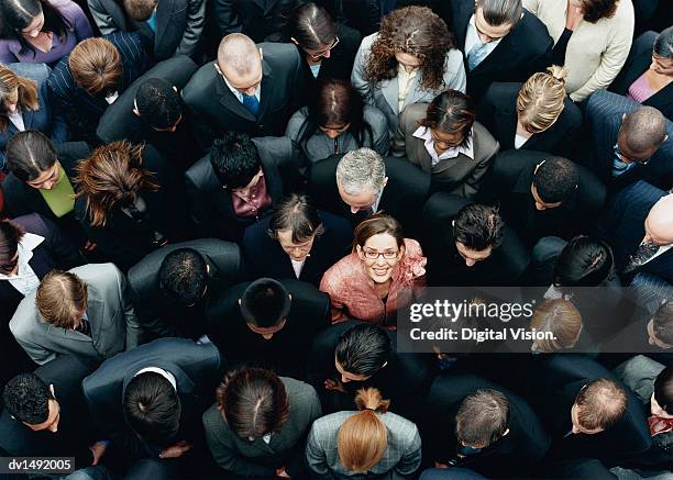 businesswoman looking up at camera and standing outdoors surrounded by a large group of business people - individualidad fotografías e imágenes de stock