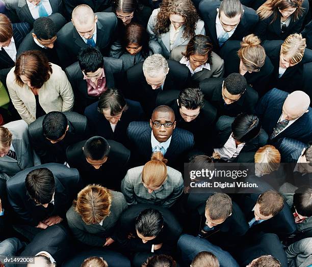 businessman looking up at camera and standing outdoors surrounded by a large group of business people - individuality fotografías e imágenes de stock