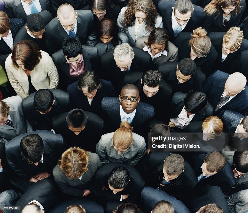 Businessman Looking up at Camera and Standing Outdoors Surrounded by a Large Group of Business People