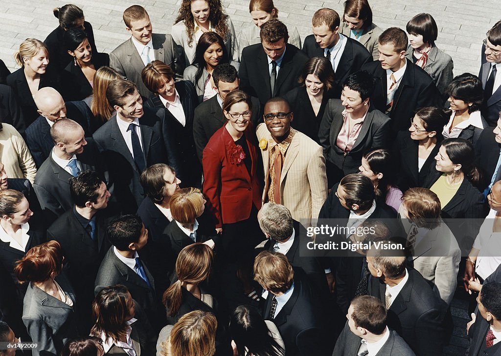 Businessman and Businesswoman Standing Outdoors Surrounded by a Large Group of Business People